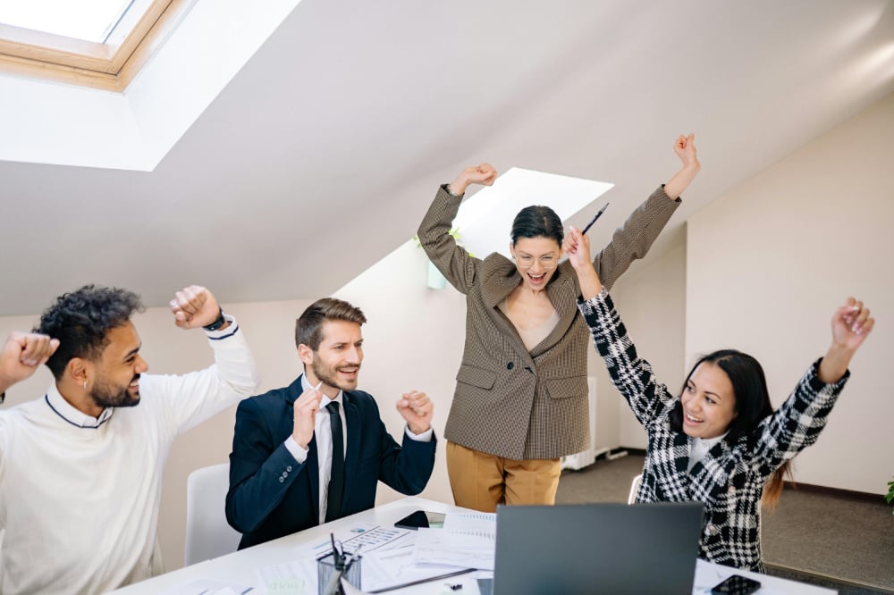 Group of office workers celebrating in front of a laptop.