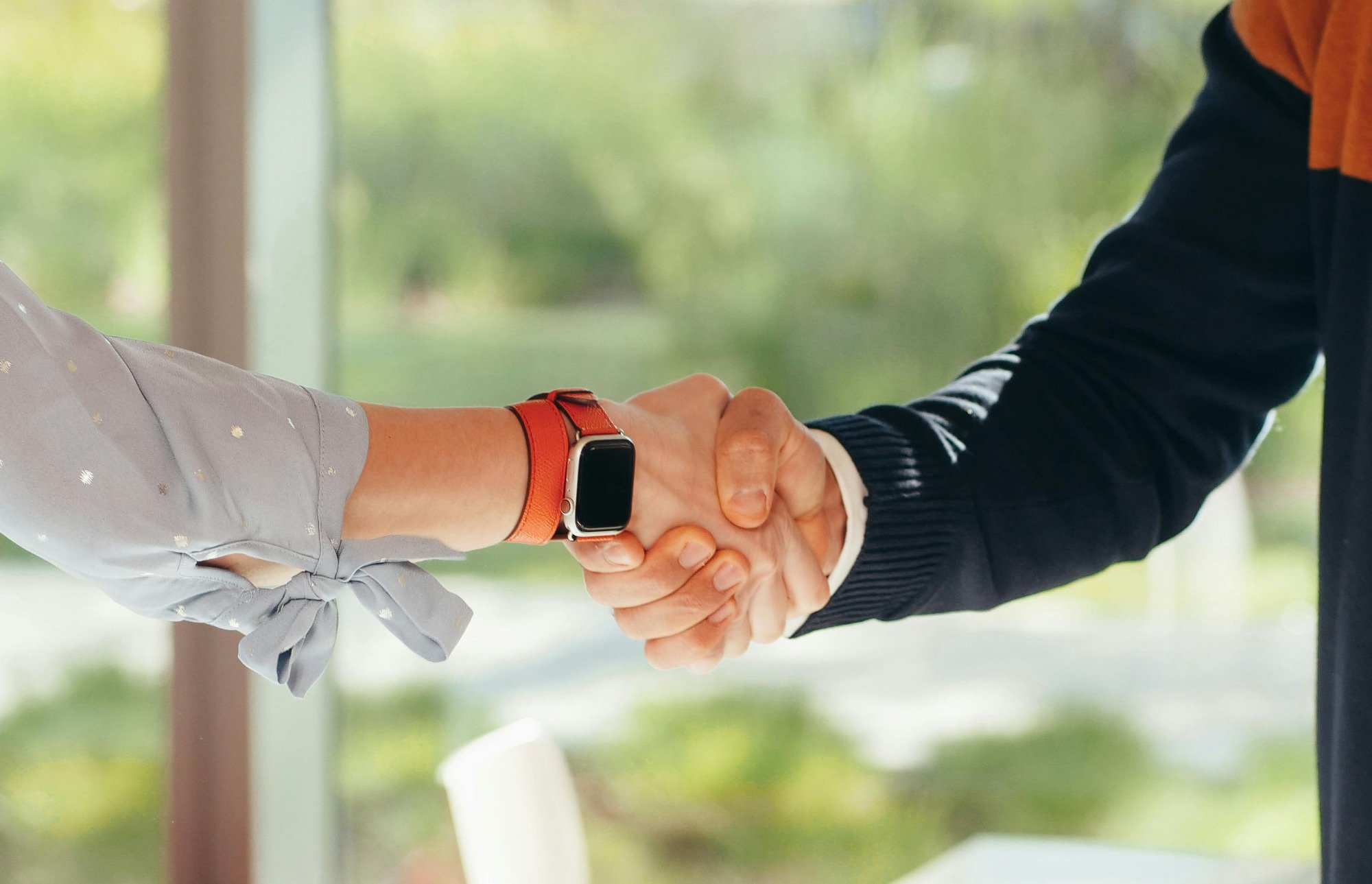 Two people shaking hands in front of green background.