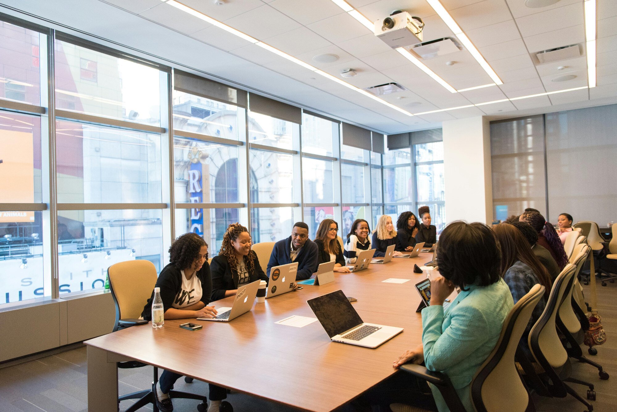 Lots of people sitting around a long office desk having a meeting.