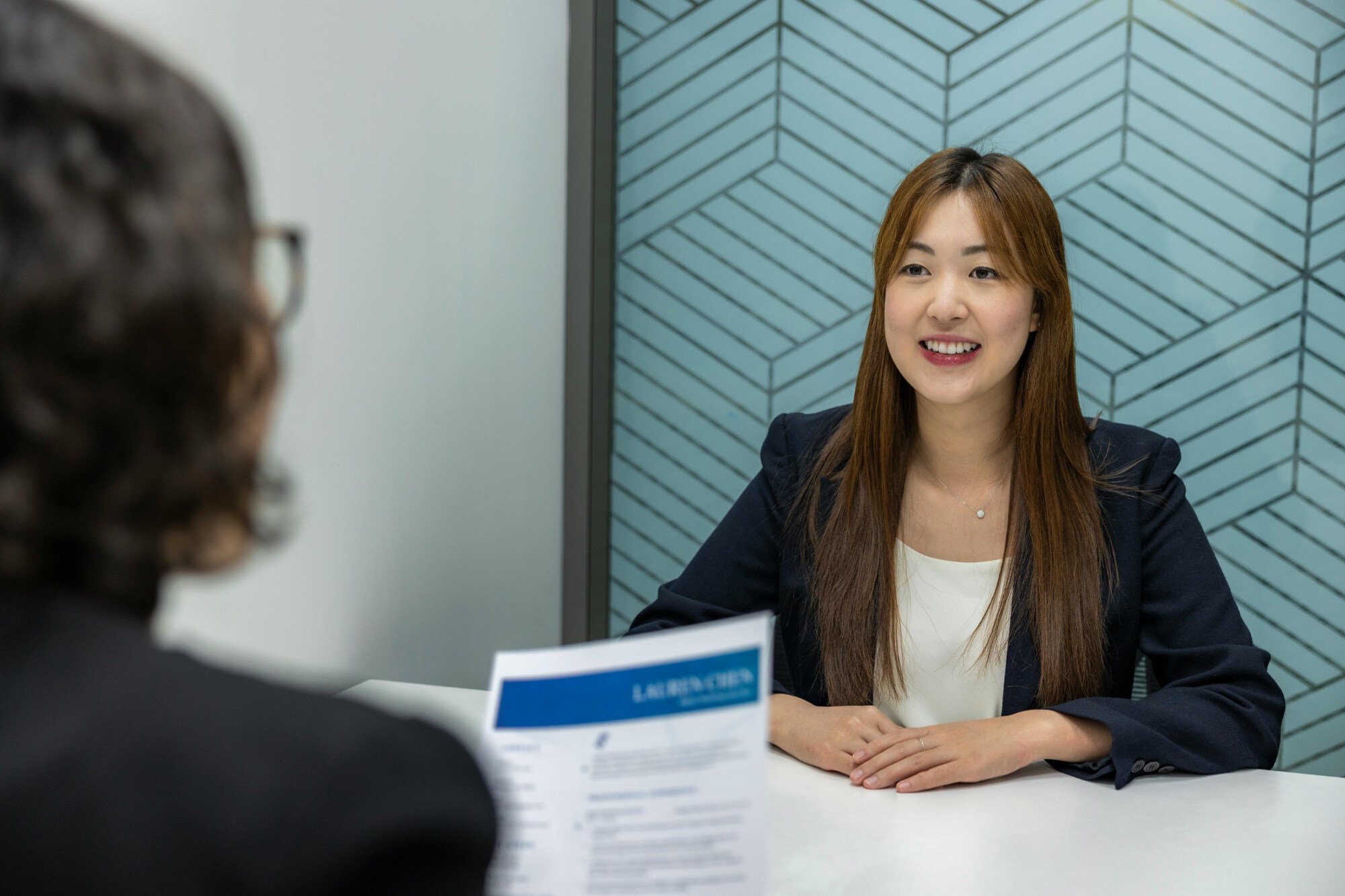 An interviewee facing a single interviewer with CV in their hand.