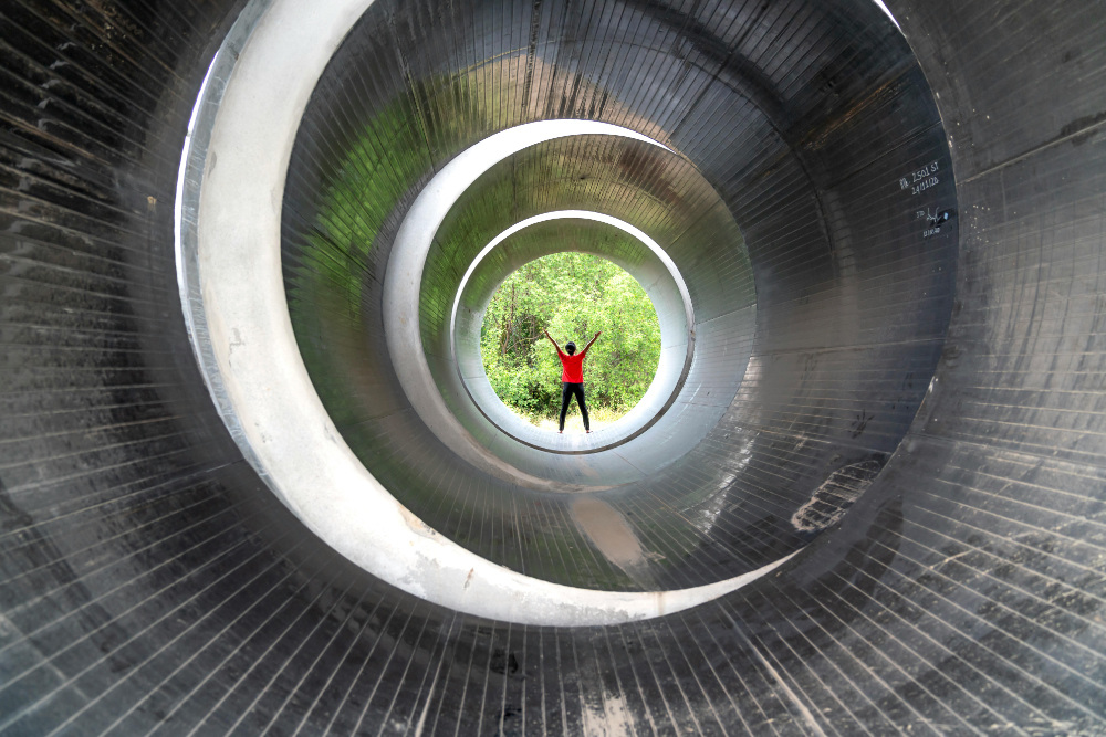 Person standing at the end of metal tunnel looking out at the forest.