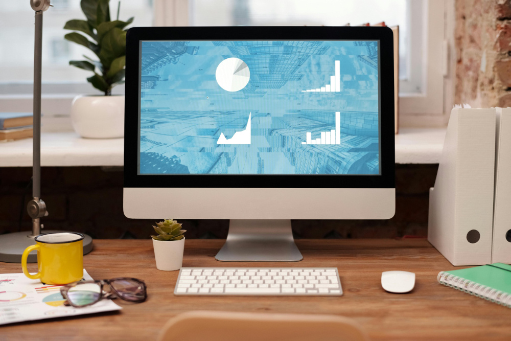 iMac on wooden desk with various charts visible on the screen.